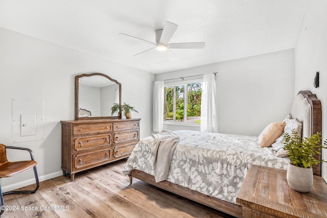 bedroom featuring ceiling fan, light hardwood / wood-style floors, and electric panel