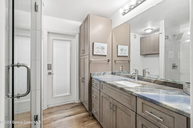 bathroom with a shower with door, hardwood / wood-style flooring, a textured ceiling, and vanity