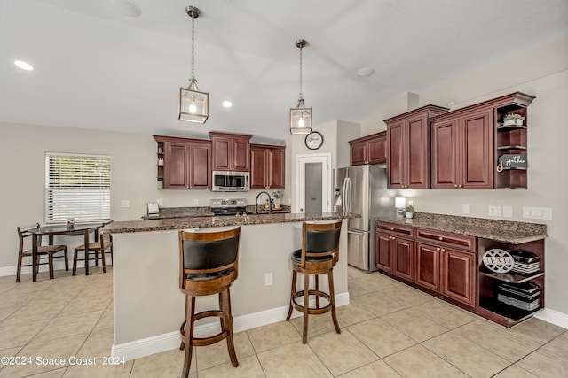 kitchen featuring a kitchen bar, stainless steel appliances, light tile patterned floors, a center island with sink, and hanging light fixtures