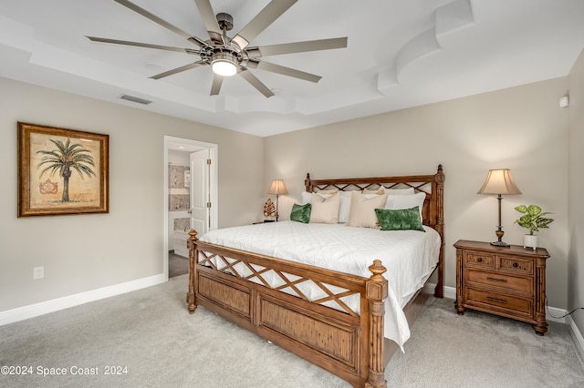 carpeted bedroom with a raised ceiling, ensuite bath, and ceiling fan