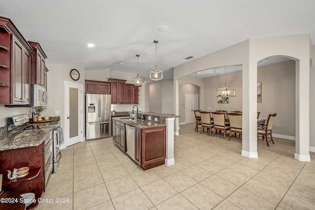 kitchen featuring sink, dark stone countertops, an island with sink, decorative light fixtures, and appliances with stainless steel finishes