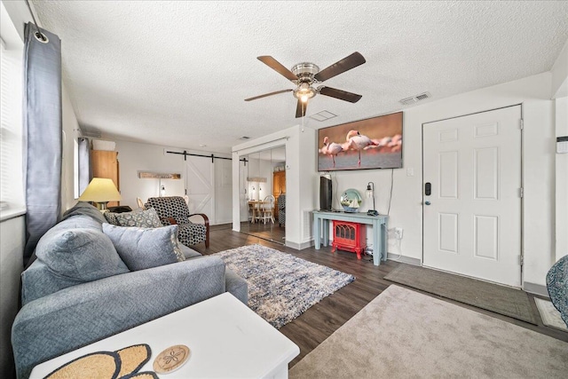 living room featuring a barn door, ceiling fan, dark wood-type flooring, and a textured ceiling