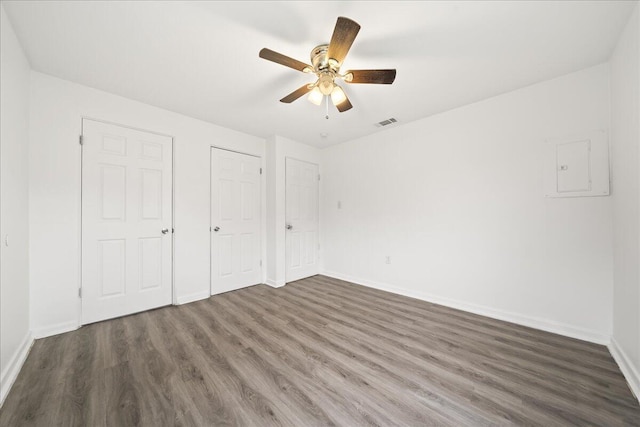 unfurnished bedroom with multiple closets, ceiling fan, dark hardwood / wood-style flooring, and electric panel