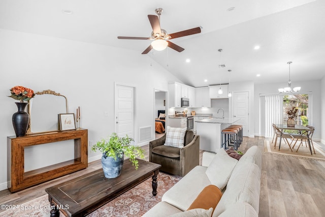 living room featuring sink, light wood-type flooring, ceiling fan with notable chandelier, and high vaulted ceiling