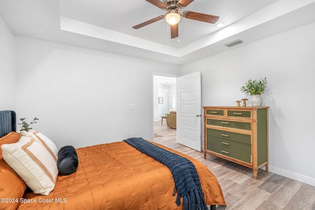 bedroom with ceiling fan, light hardwood / wood-style floors, and a tray ceiling