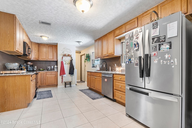 kitchen featuring sink, light tile patterned floors, a textured ceiling, appliances with stainless steel finishes, and light stone counters