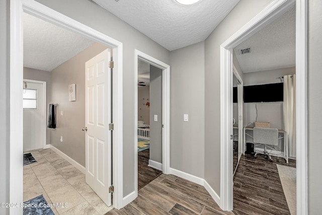 corridor with a textured ceiling and light hardwood / wood-style floors