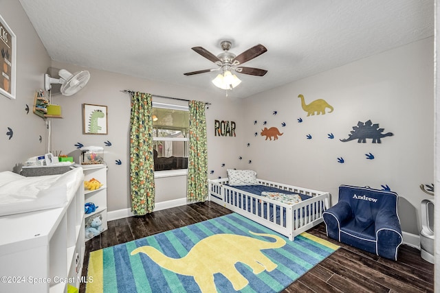 bedroom with a textured ceiling, ceiling fan, dark wood-type flooring, and a nursery area