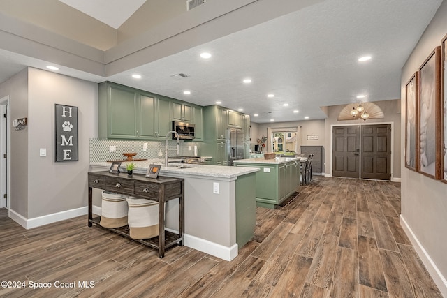 kitchen featuring green cabinets, a kitchen island with sink, dark wood-type flooring, and decorative backsplash