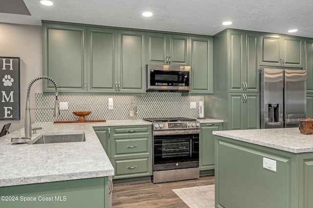 kitchen featuring hardwood / wood-style flooring, an island with sink, appliances with stainless steel finishes, and green cabinetry