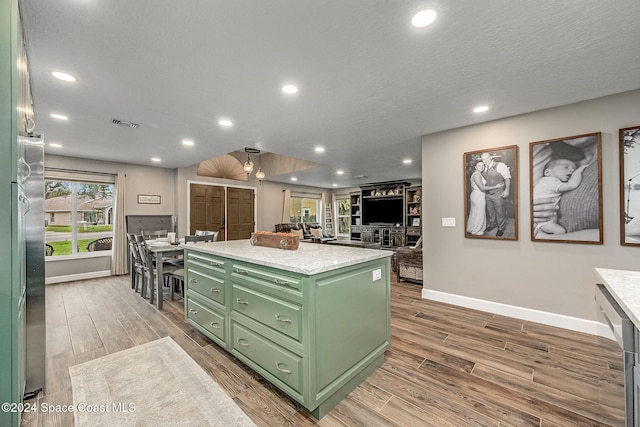 kitchen with a textured ceiling, ceiling fan, light hardwood / wood-style flooring, green cabinetry, and a kitchen island