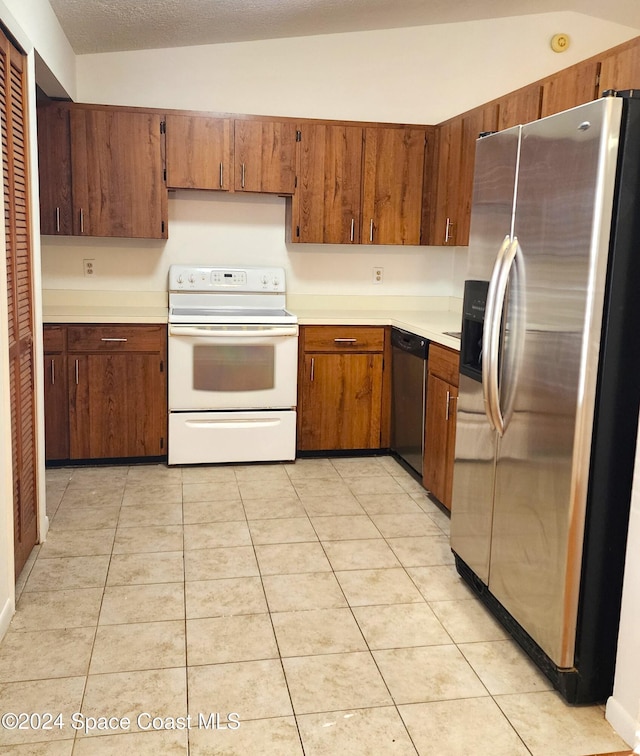 kitchen featuring light tile patterned floors, a textured ceiling, appliances with stainless steel finishes, and vaulted ceiling