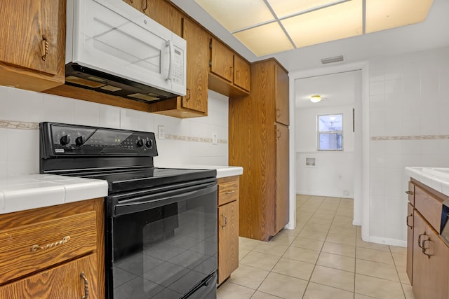 kitchen featuring tile countertops, light tile patterned flooring, backsplash, and black / electric stove