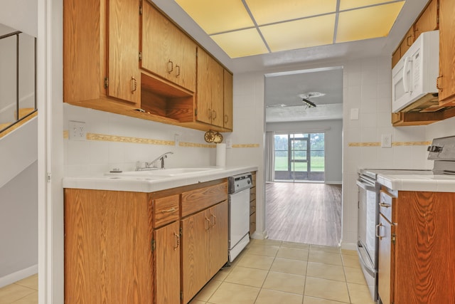 kitchen with sink, backsplash, white appliances, light tile patterned floors, and tile walls