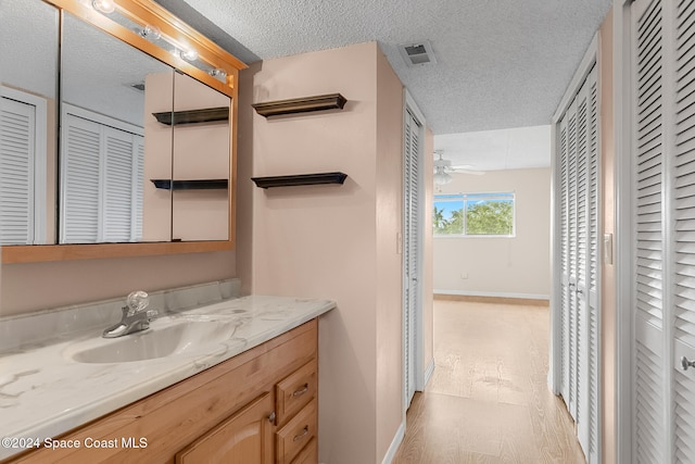 bathroom with hardwood / wood-style floors, vanity, ceiling fan, and a textured ceiling