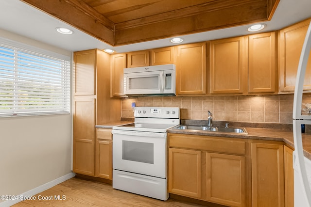 kitchen with backsplash, white appliances, a raised ceiling, sink, and light hardwood / wood-style flooring