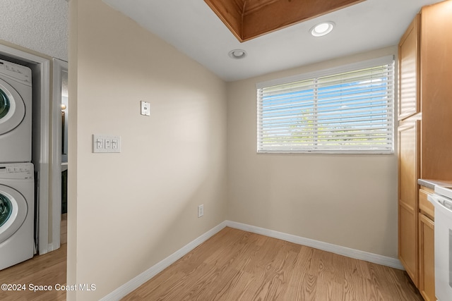 washroom with light hardwood / wood-style floors and stacked washing maching and dryer