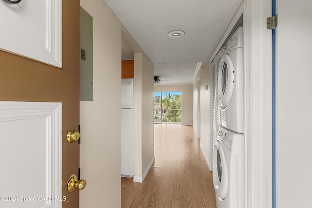 washroom with a textured ceiling, ceiling fan, stacked washer / drying machine, and light wood-type flooring