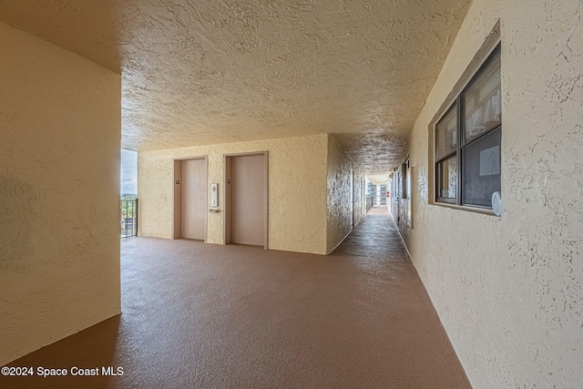 hallway with a textured ceiling and dark colored carpet