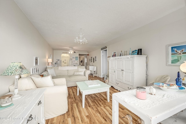 living room featuring ceiling fan with notable chandelier, a textured ceiling, and light hardwood / wood-style flooring