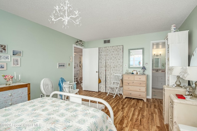 bedroom with a textured ceiling, light wood-type flooring, ensuite bath, and a notable chandelier