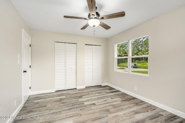 unfurnished bedroom featuring ceiling fan, light hardwood / wood-style flooring, and multiple closets