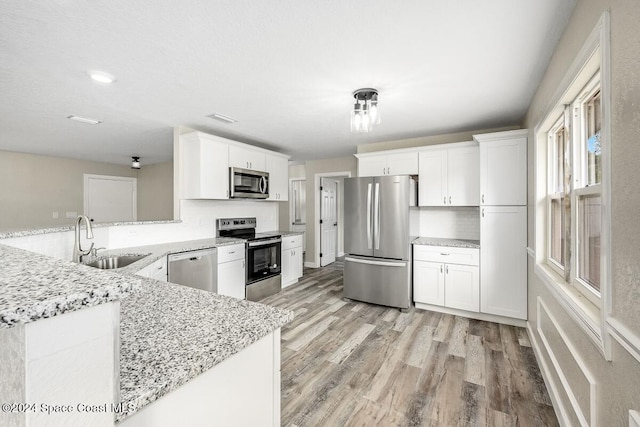 kitchen featuring kitchen peninsula, appliances with stainless steel finishes, sink, light hardwood / wood-style floors, and white cabinetry