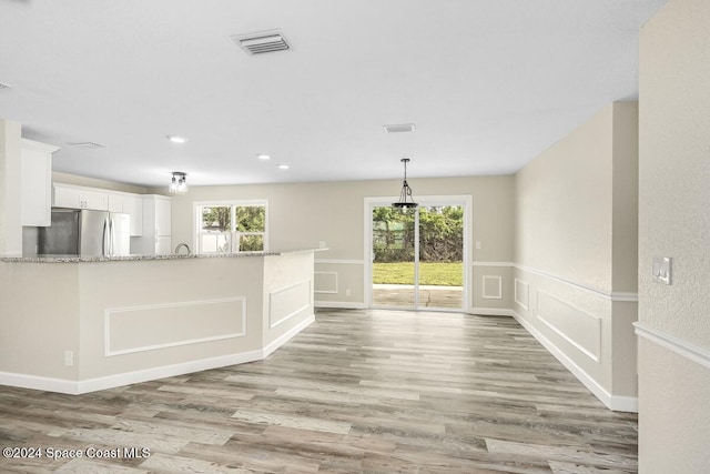 kitchen with stainless steel refrigerator, light stone countertops, white cabinets, and a healthy amount of sunlight