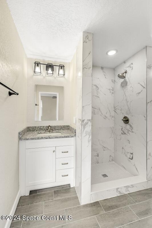 bathroom with a textured ceiling, vanity, and tiled shower