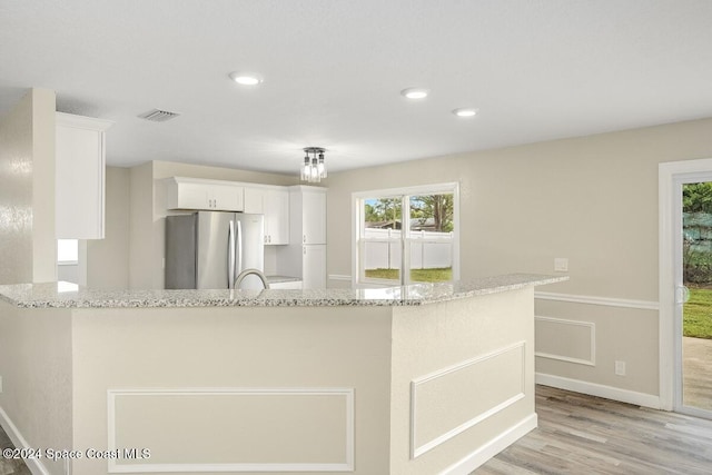 kitchen with white cabinets, sink, light stone countertops, light wood-type flooring, and stainless steel refrigerator