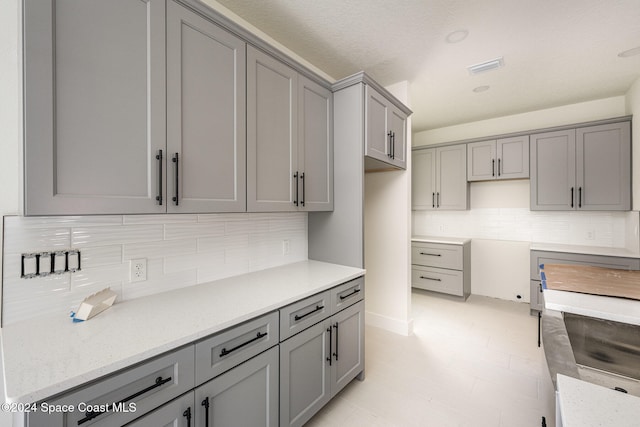 kitchen featuring gray cabinets, light stone counters, and tasteful backsplash