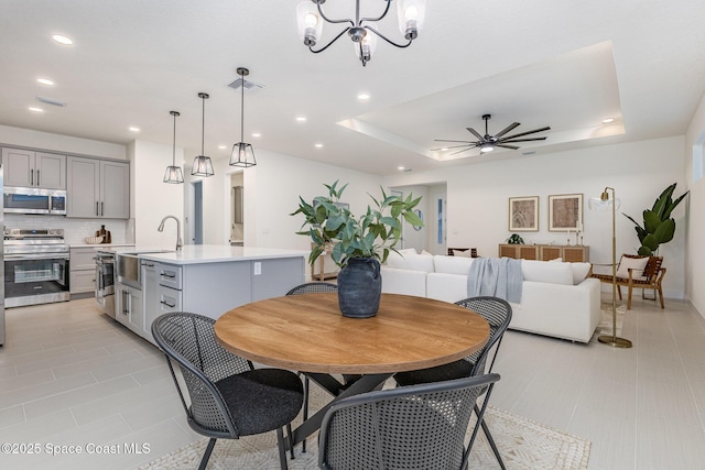 tiled dining space with sink, ceiling fan with notable chandelier, and a raised ceiling