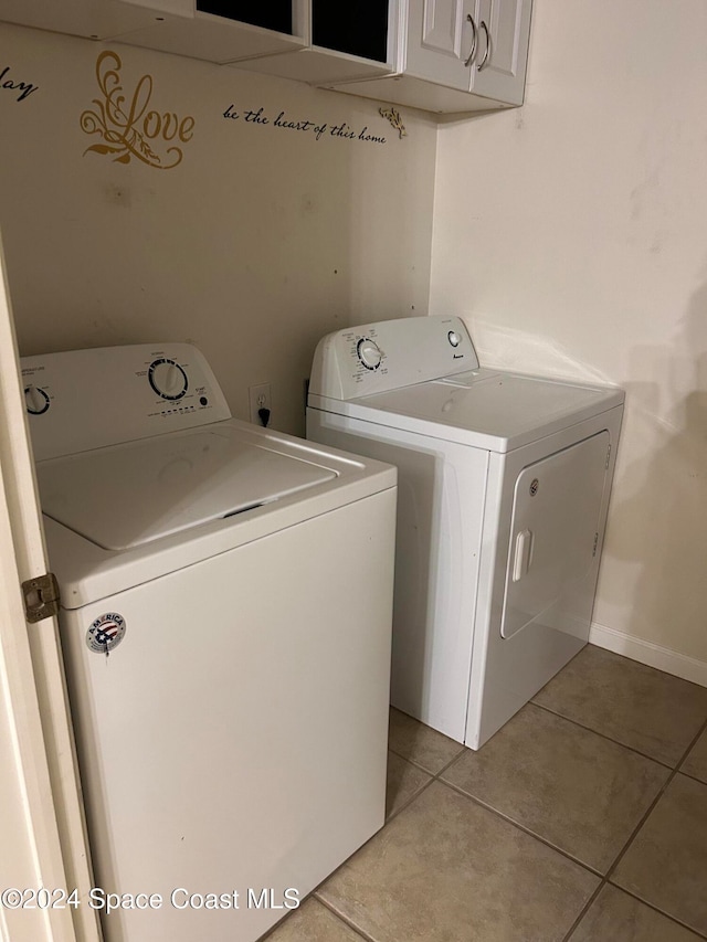 clothes washing area featuring washing machine and clothes dryer, light tile patterned floors, and cabinets