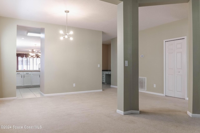 spare room featuring light colored carpet and an inviting chandelier