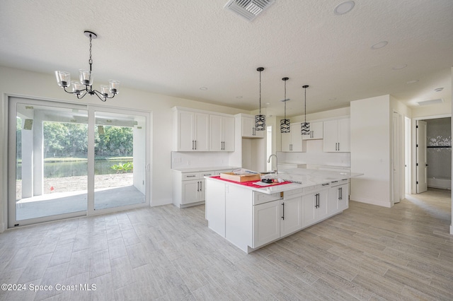 kitchen featuring pendant lighting, white cabinets, an island with sink, and light hardwood / wood-style floors