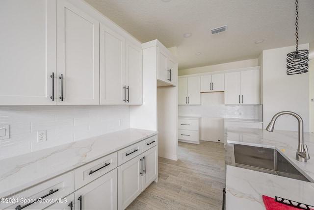 kitchen featuring white cabinets, light wood-type flooring, decorative light fixtures, and light stone countertops