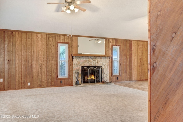 unfurnished living room with ceiling fan, a stone fireplace, and carpet flooring