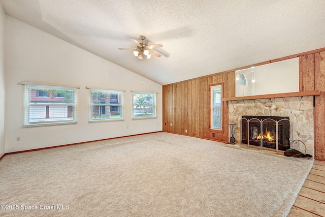 unfurnished living room with ceiling fan, a wealth of natural light, a stone fireplace, and wooden walls