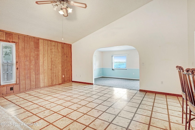 tiled spare room featuring ceiling fan, wood walls, and lofted ceiling