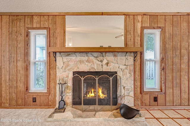 room details featuring carpet, a stone fireplace, wood walls, and a textured ceiling