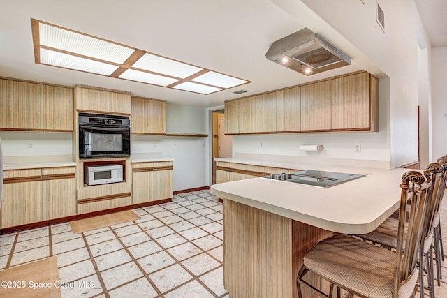 kitchen with black appliances, kitchen peninsula, light brown cabinets, and a breakfast bar area