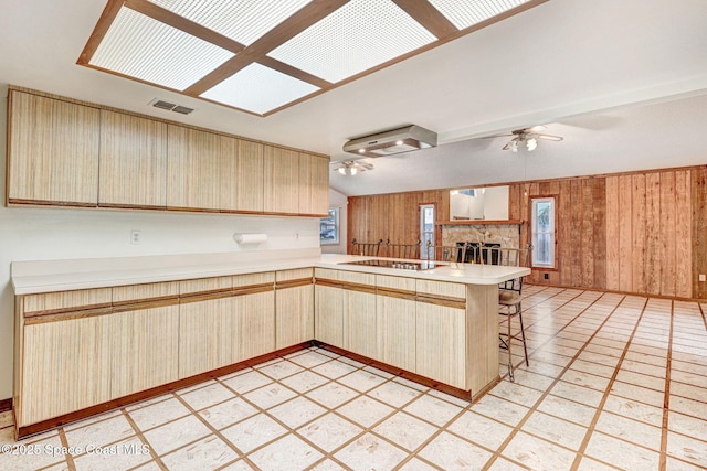 kitchen featuring light brown cabinetry, kitchen peninsula, ceiling fan, black electric cooktop, and a breakfast bar area