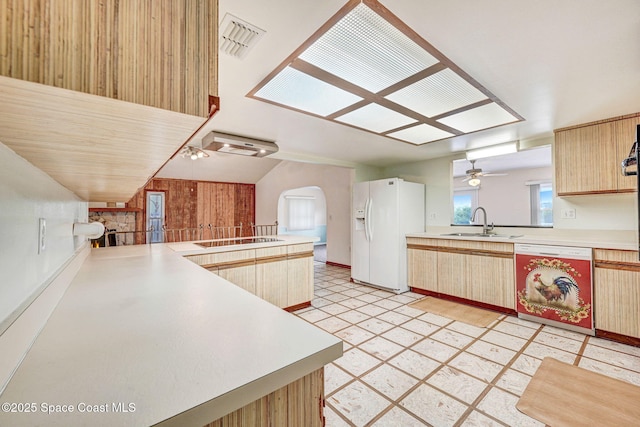 kitchen featuring dishwasher, wood walls, kitchen peninsula, sink, and white fridge with ice dispenser