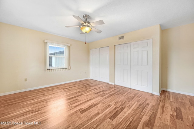 unfurnished bedroom with ceiling fan, two closets, and light hardwood / wood-style floors