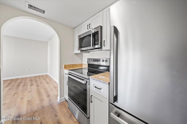 kitchen with light stone counters, white cabinetry, stainless steel appliances, and light hardwood / wood-style flooring