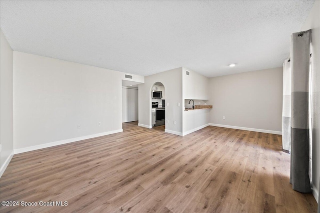 unfurnished living room featuring a textured ceiling, sink, and light hardwood / wood-style flooring