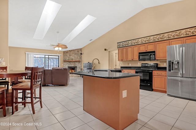 kitchen featuring a skylight, sink, black appliances, light tile patterned floors, and a fireplace