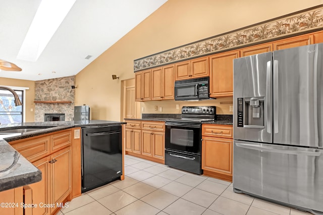 kitchen featuring a skylight, dark stone counters, sink, black appliances, and light tile patterned floors