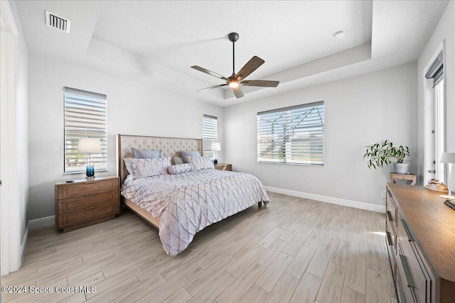 bedroom featuring light wood-type flooring, a tray ceiling, and ceiling fan