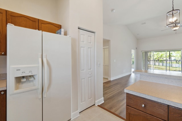 kitchen with white fridge with ice dispenser, hanging light fixtures, light hardwood / wood-style flooring, a notable chandelier, and lofted ceiling